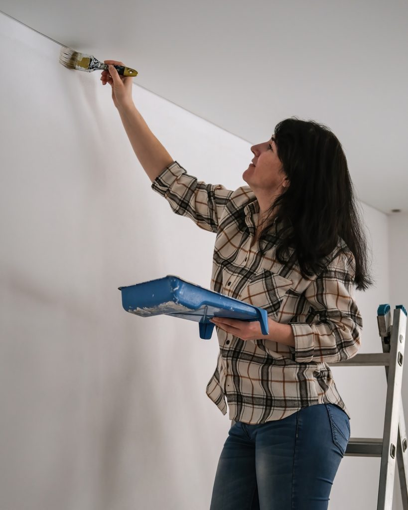 Woman painting a wall with white paint